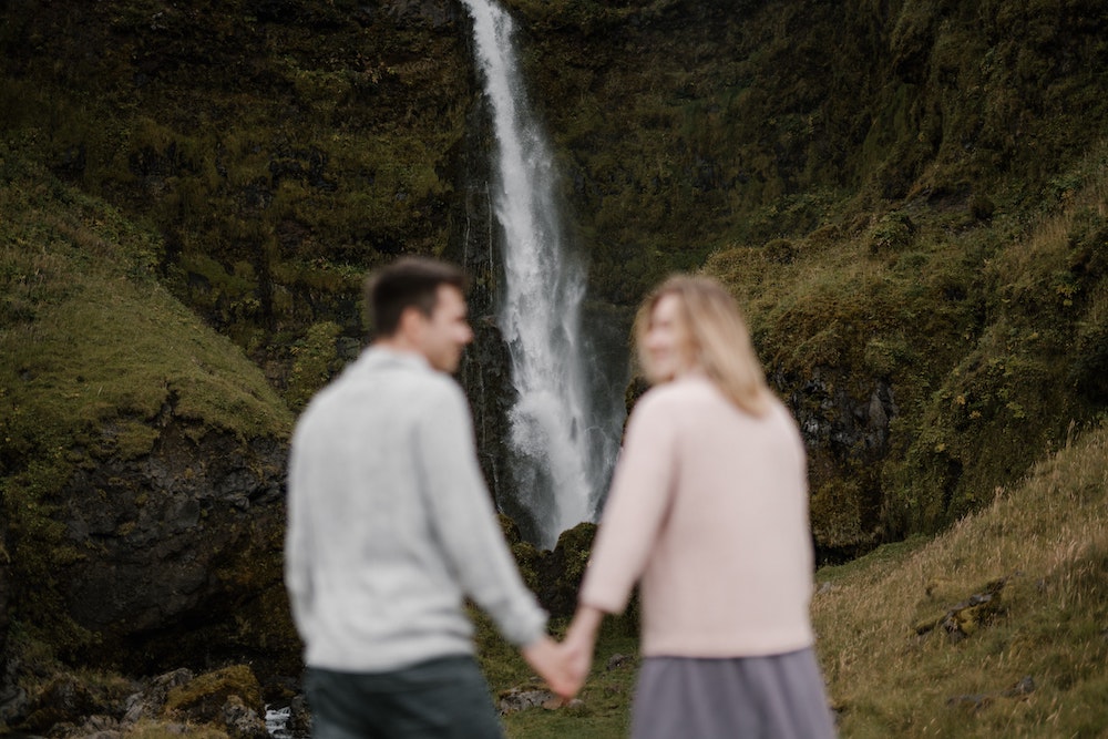 A couple hand in hand hiking to a waterfall